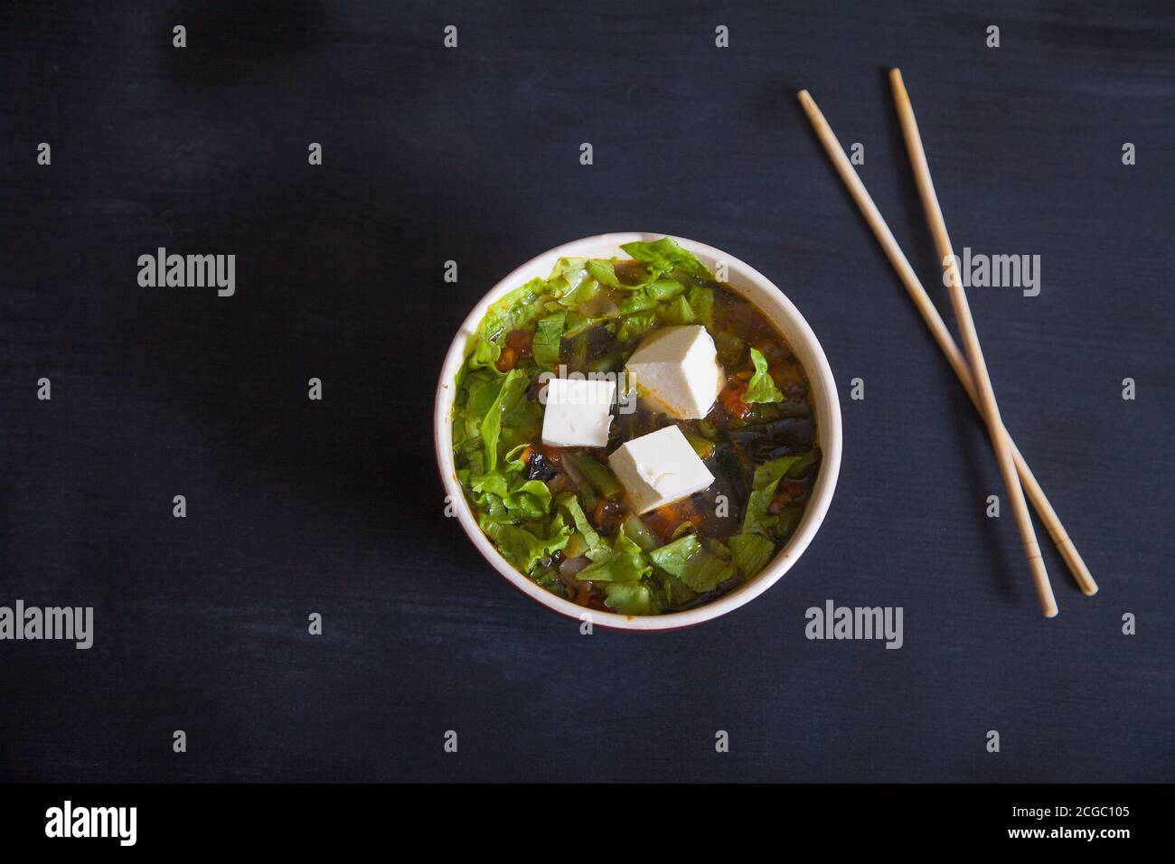 Sopa japonesa con queso tofu, judías verdes, verduras, hierbas, palillos de bambú sobre fondo negro. Copiar espas Foto de stock