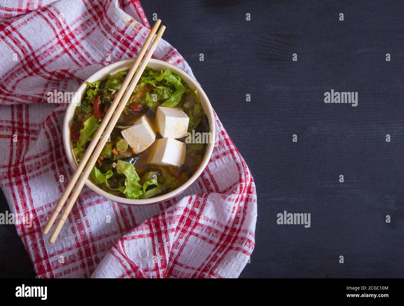 Sopa japonesa con queso tofu, judías verdes, verduras, hierbas, palillos de bambú sobre una servilleta roja sobre fondo negro. Copiar espas Foto de stock