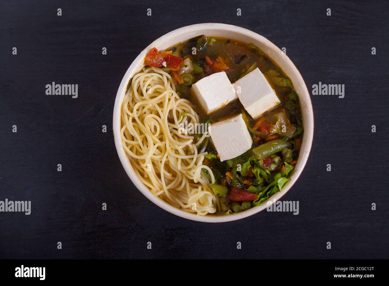 Sopa japonesa con tofu, fideos, verduras y hierbas, sobre fondo negro. Copiar espas Foto de stock