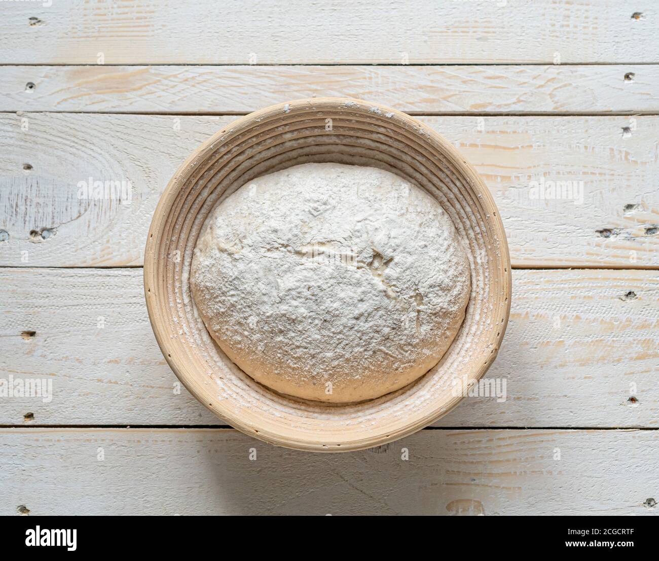 Masa de pan de masa fermentada en panleton de mimbre que prueba la cesta en madera antecedentes Foto de stock