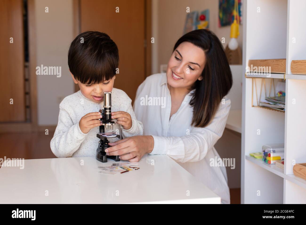Lillte Kid explorando la ciencia con un microscopio y ayuda de madre o maestro. Resolución de problemas en casa. Comunidad de aprendizaje. Escuela Montessori Foto de stock