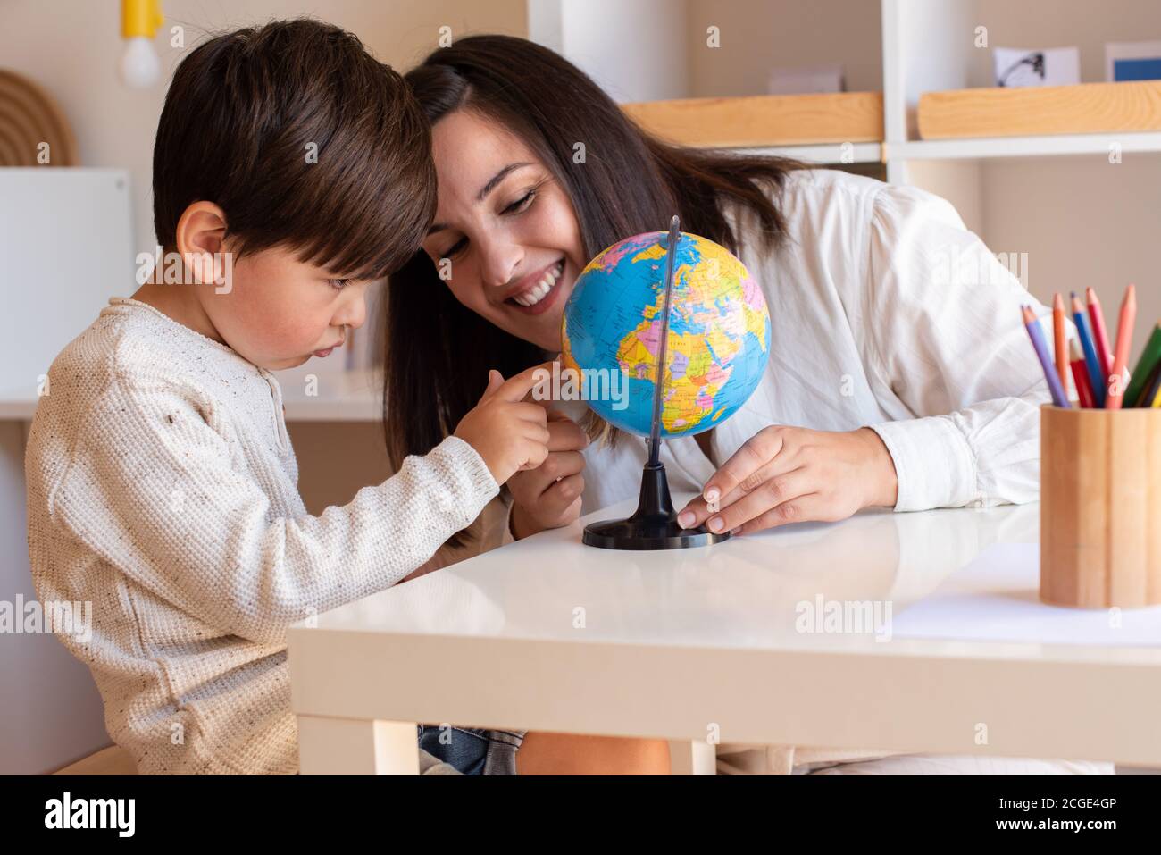 Liltle Preschooler Kid aprendiendo geografía con un mapa del globo y la ayuda del educador del profesor. Resolución de problemas en casa. Comunidad de aprendizaje. Escuela Montessori Foto de stock