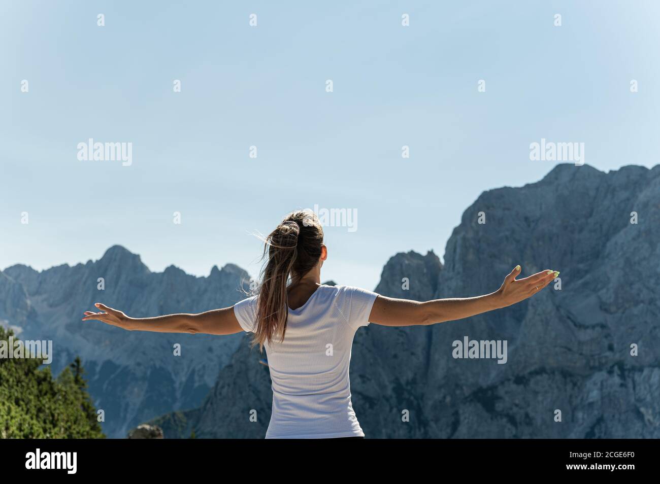 Vista desde atrás de una joven caminadora disfrutando de la vida con los brazos abiertos disfrutando de la vista de los Alpes. Foto de stock