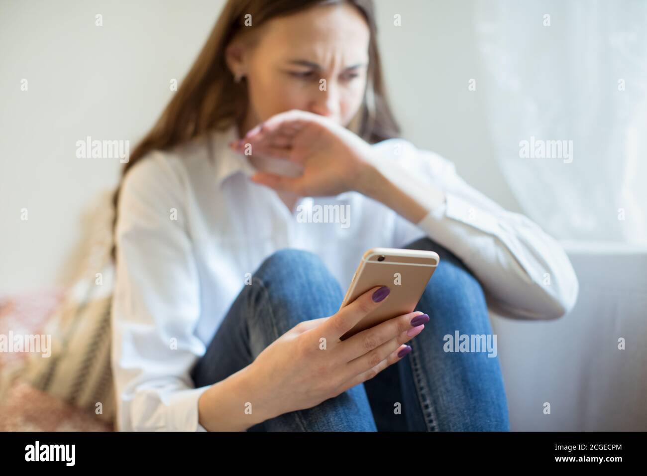 Llorando a una mujer joven en depresión mirando el teléfono recibe malas noticias, cubriendo la boca con la mano. Chica triste preocupada recibiendo mal mensaje. Emociones negativas Foto de stock