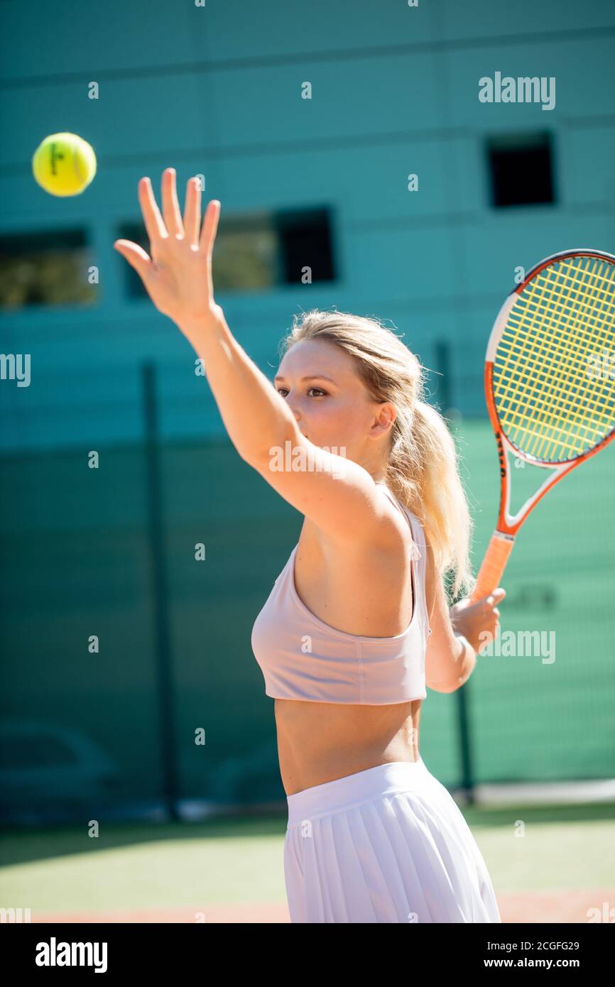 Chica atlética deportiva vistiendo ropa de tenis deportes de verano sirviendo la pelota en juego de tenis en el tribunal exterior. Foto de stock