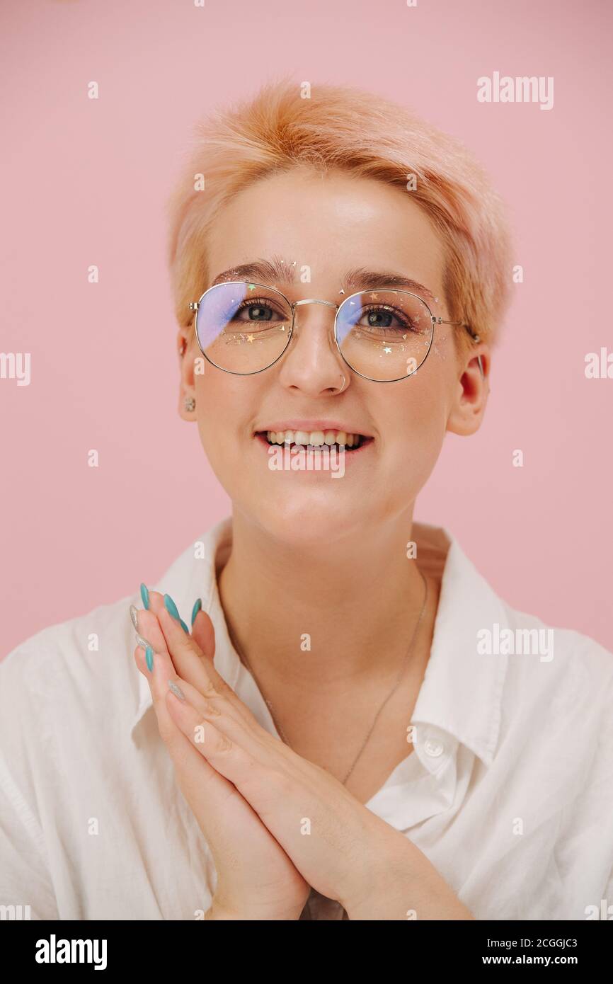 Linda mujer joven feliz con pelo corto rubio, gafas redondas y maquillaje  de ojos de estrellas Fotografía de stock - Alamy