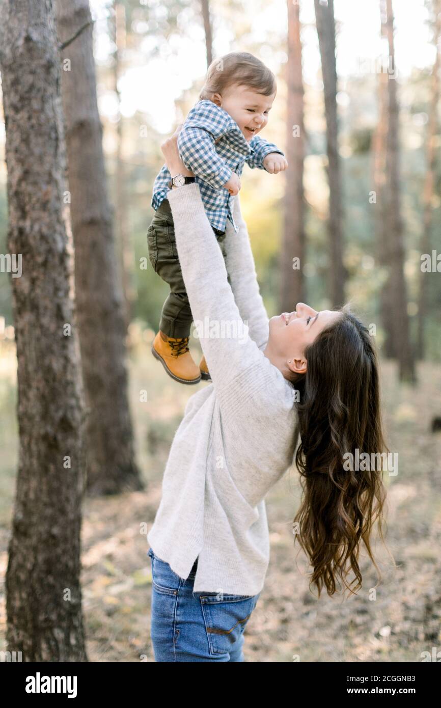 Retrato de feliz madre caucásica levantándose y jugando con su lindo hijo, disfrutando de su paseo conjunto en el bosque de pinos juntos. Feliz familia Foto de stock