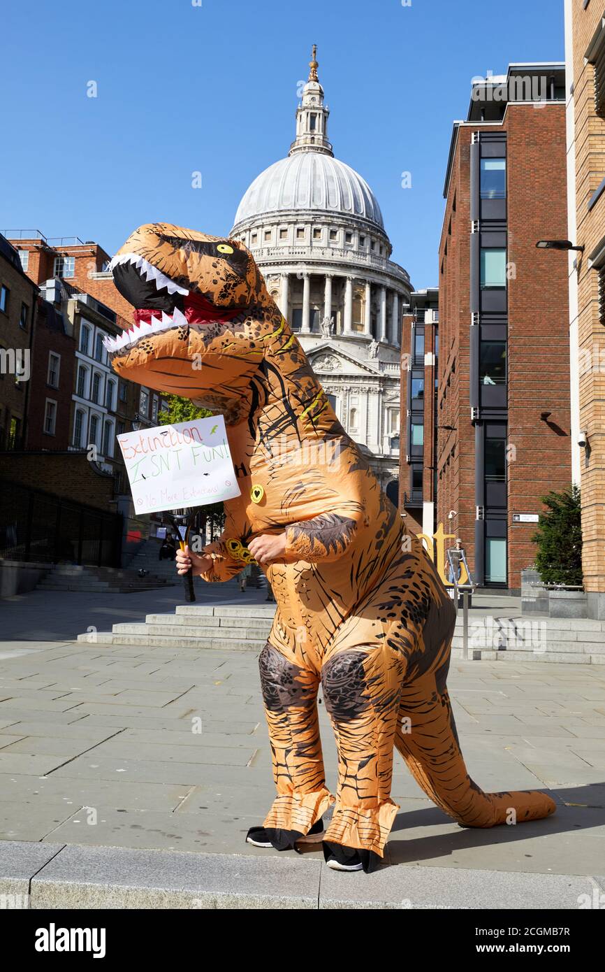 2020: Un defensor de la Rebelión de extinción, vestido con un traje de dinosaurio, se encuentra fuera de la Catedral de San Pablo durante una marcha por el grupo. Foto de stock