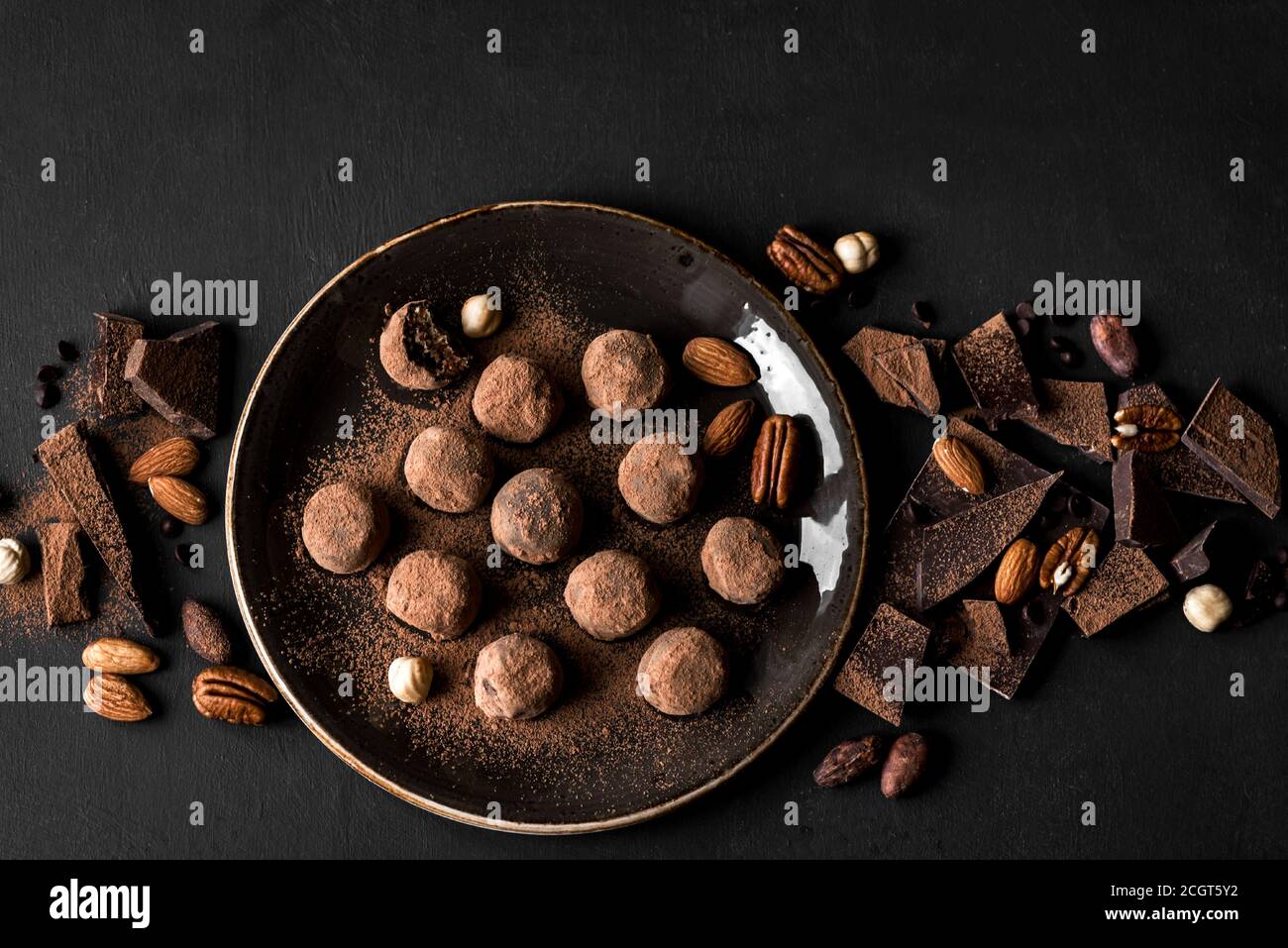 Trufas de chocolate con chocolate negro y nueces sobre fondo negro, vista superior, espacio de copia. Bolas de energía de chocolate caseras veganas o trufas para desse Foto de stock