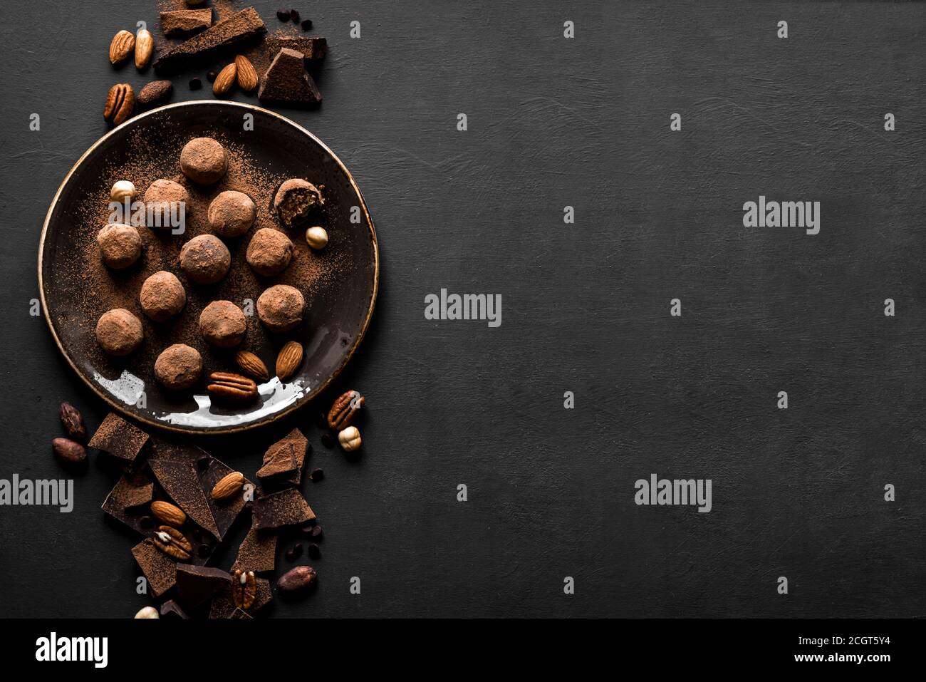 Trufas de chocolate con chocolate negro y nueces sobre fondo negro, vista superior, espacio de copia. Bolas de energía de chocolate caseras veganas o trufas para desse Foto de stock