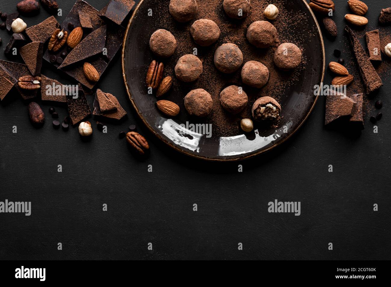 Trufas de chocolate con chocolate negro y nueces sobre fondo negro, vista superior, espacio de copia. Bolas de energía de chocolate caseras veganas o trufas para desse Foto de stock