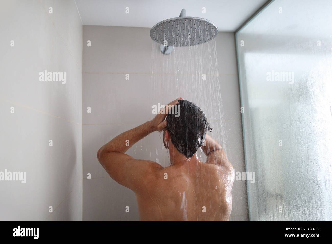 Hombre tomando una ducha lavando el cabello bajo el agua que cae de la ducha de lluvia. Persona que se ducha en el estilo de vida de casa. Cuidado corporal de adultos jóvenes rutina de mañana Foto de stock