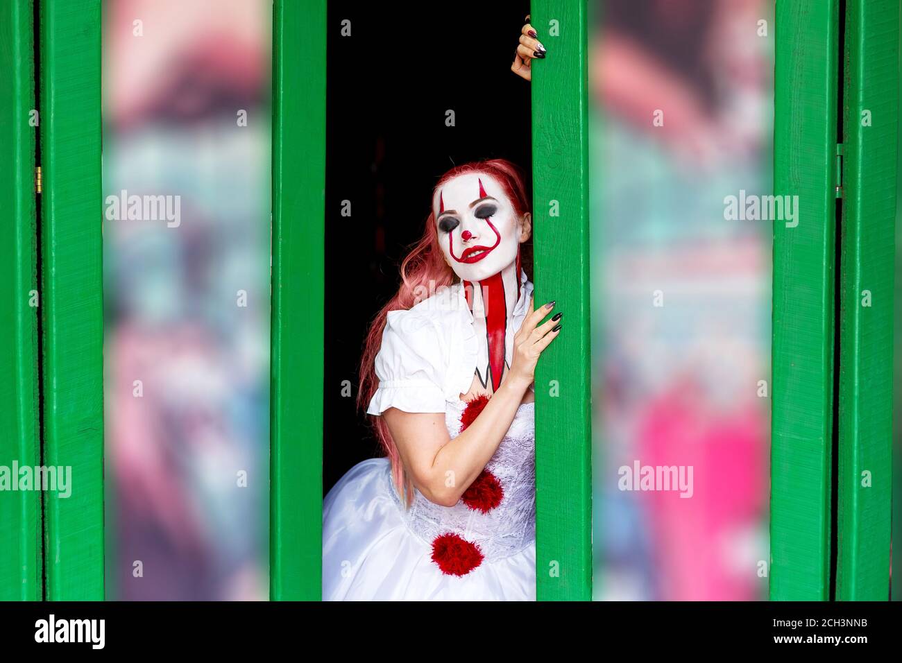 Chica con pelo largo y rojo maquillaje en su cara para Halloween en un vestido  blanco en forma de payaso se encuentra en la puerta con sus ojos cerrados,  Hallo Fotografía de