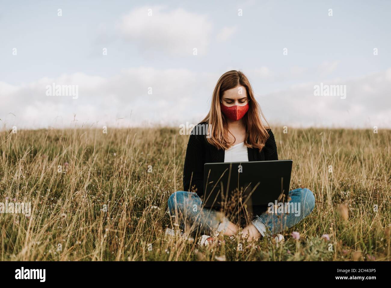 Chica con máscara utilizando un ordenador portátil en un entorno natural Foto de stock