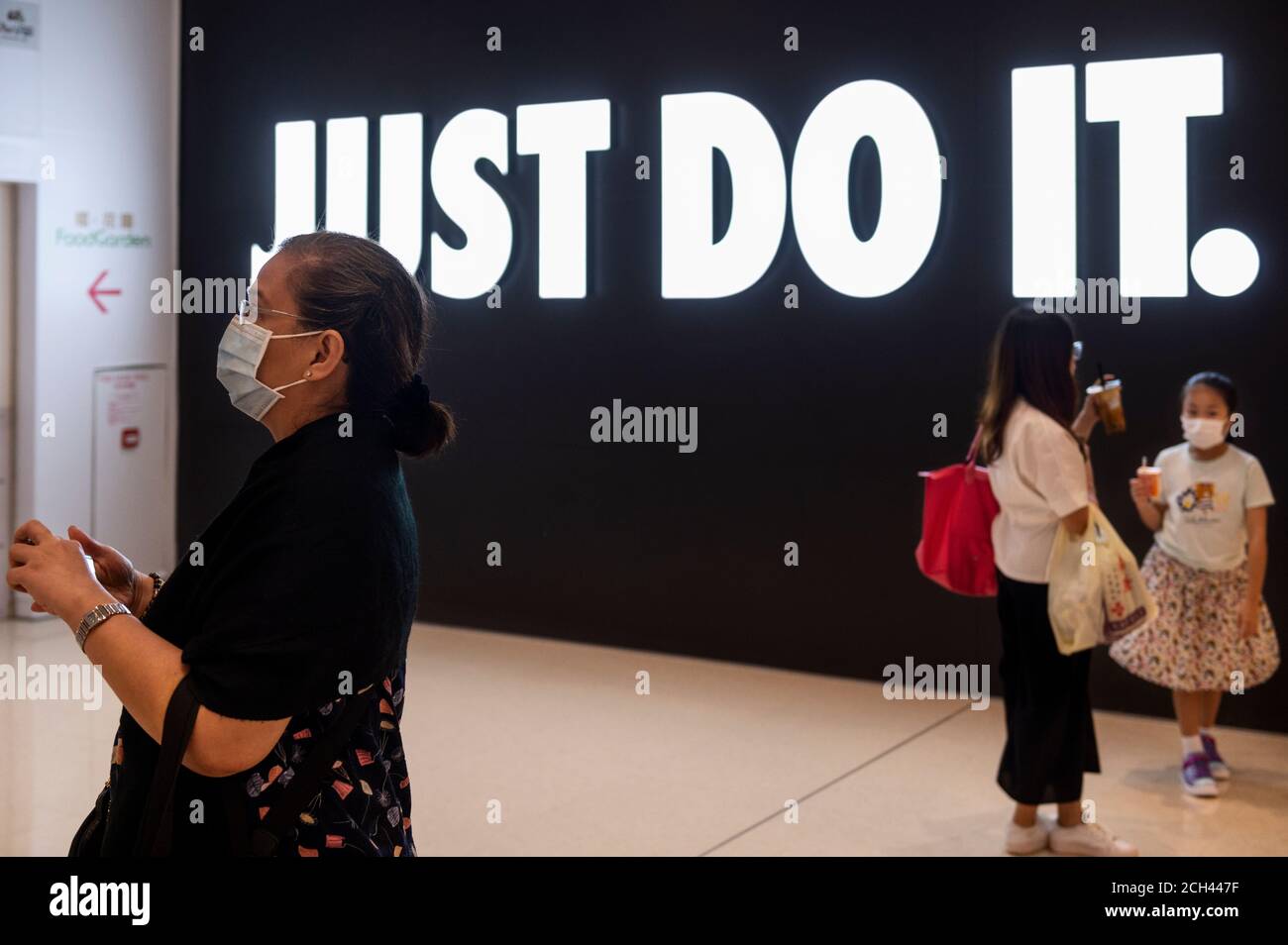 Los compradores que usan máscaras de cara pasan por una Marca multinacional  estadounidense de ropa deportiva Nike Store, logo, con un eslogan 'Just do  It' en Hong Kong Fotografía de stock -
