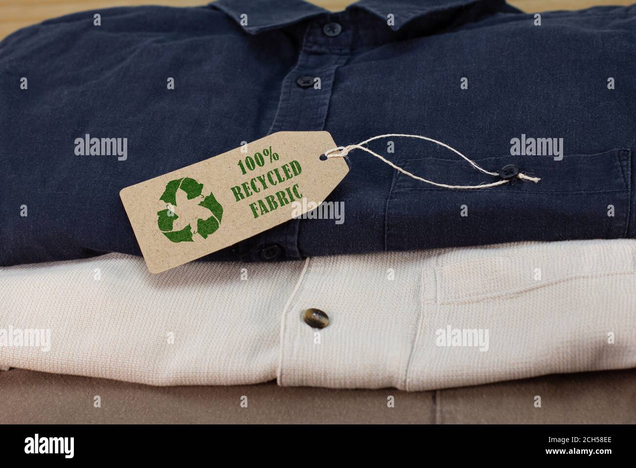 Camisas con icono de reciclaje de ropa en la etiqueta con 100% de texto de tela reciclado. Moda sostenible y compras éticas para reducir el concepto de residuos Foto de stock