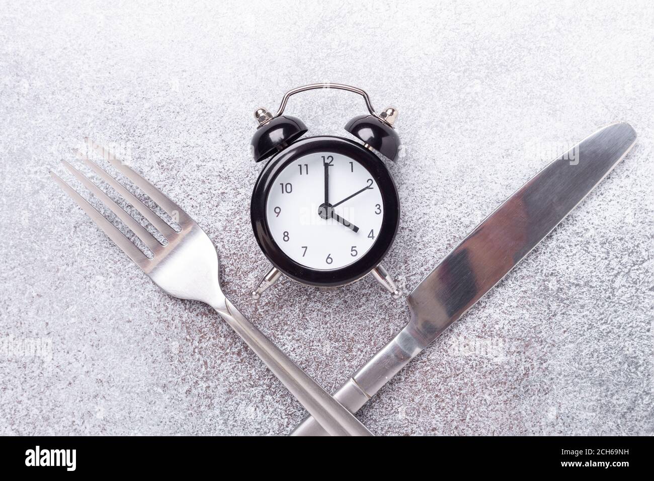 Reloj de alarma negro, tenedor, cuchillo sobre fondo oscuro. Concepto de ayuno intermitente - imagen Foto de stock