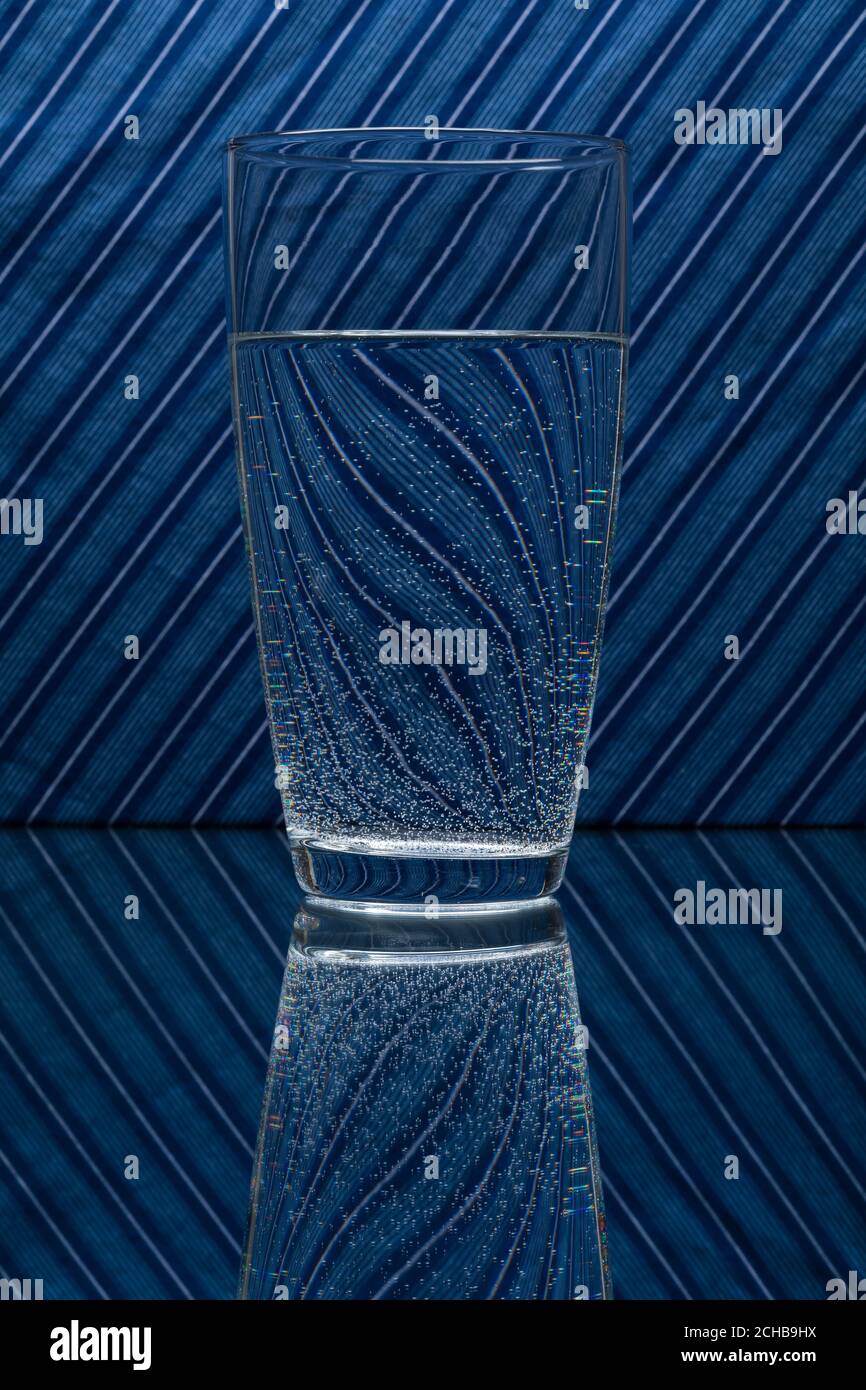 Un vaso de agua que refleja un fondo de rayas azules. Foto de stock
