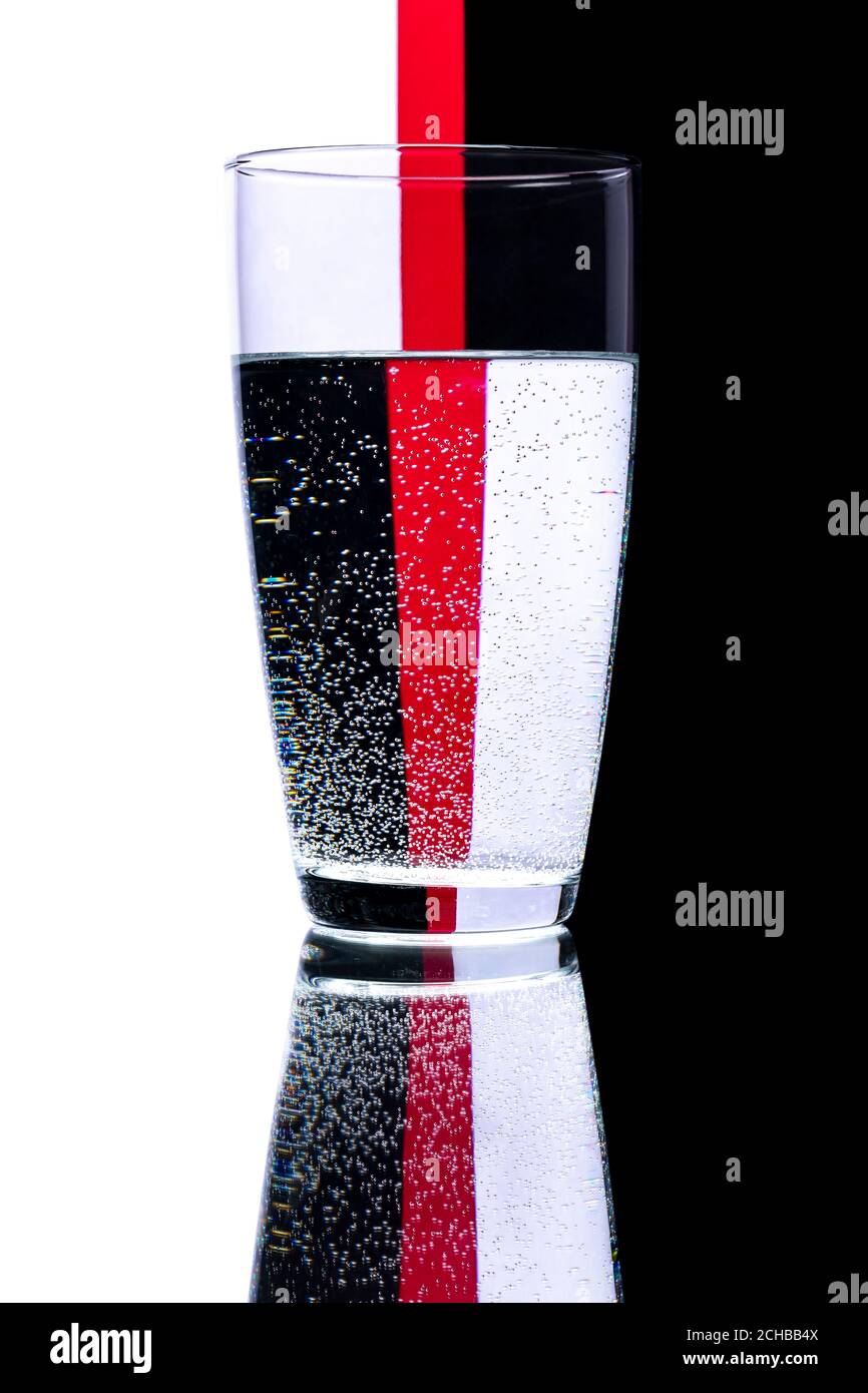 Un vaso de agua que refleja un fondo negro, blanco y rojo. Foto de stock