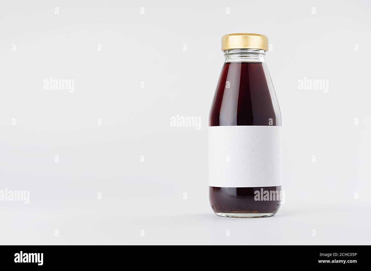 Jugo de cereza roja en botella de vidrio con tapón de oro y etiqueta blanca en blanco se mofa sobre fondo blanco con espacio de copia, plantilla para el embalaje, publicidad, Foto de stock