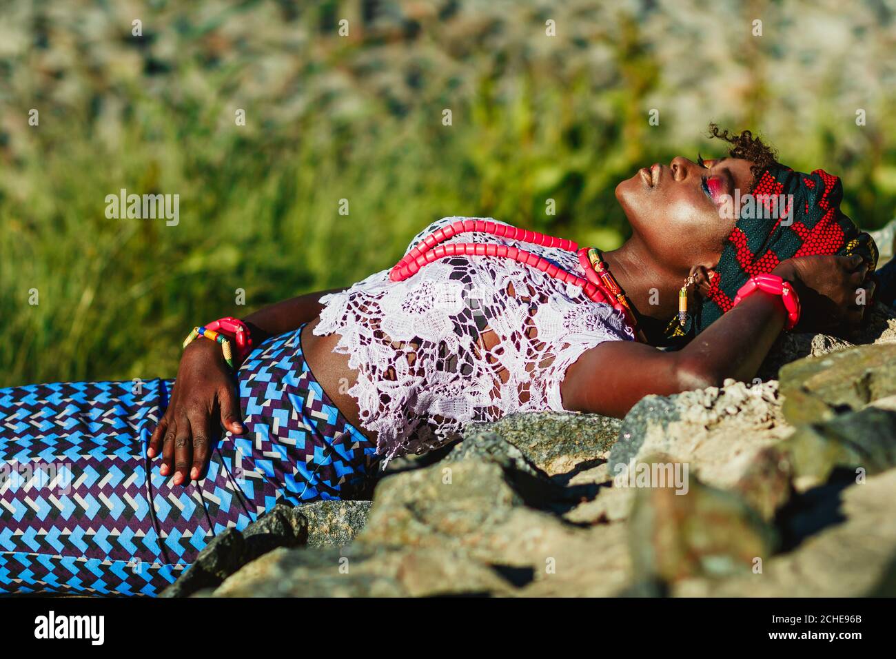 Foto de moda de modelo femenino joven africano en traje nacional, turbante y brillante de colores componen acostado en las piedras. Concepto turístico exótico Foto de stock