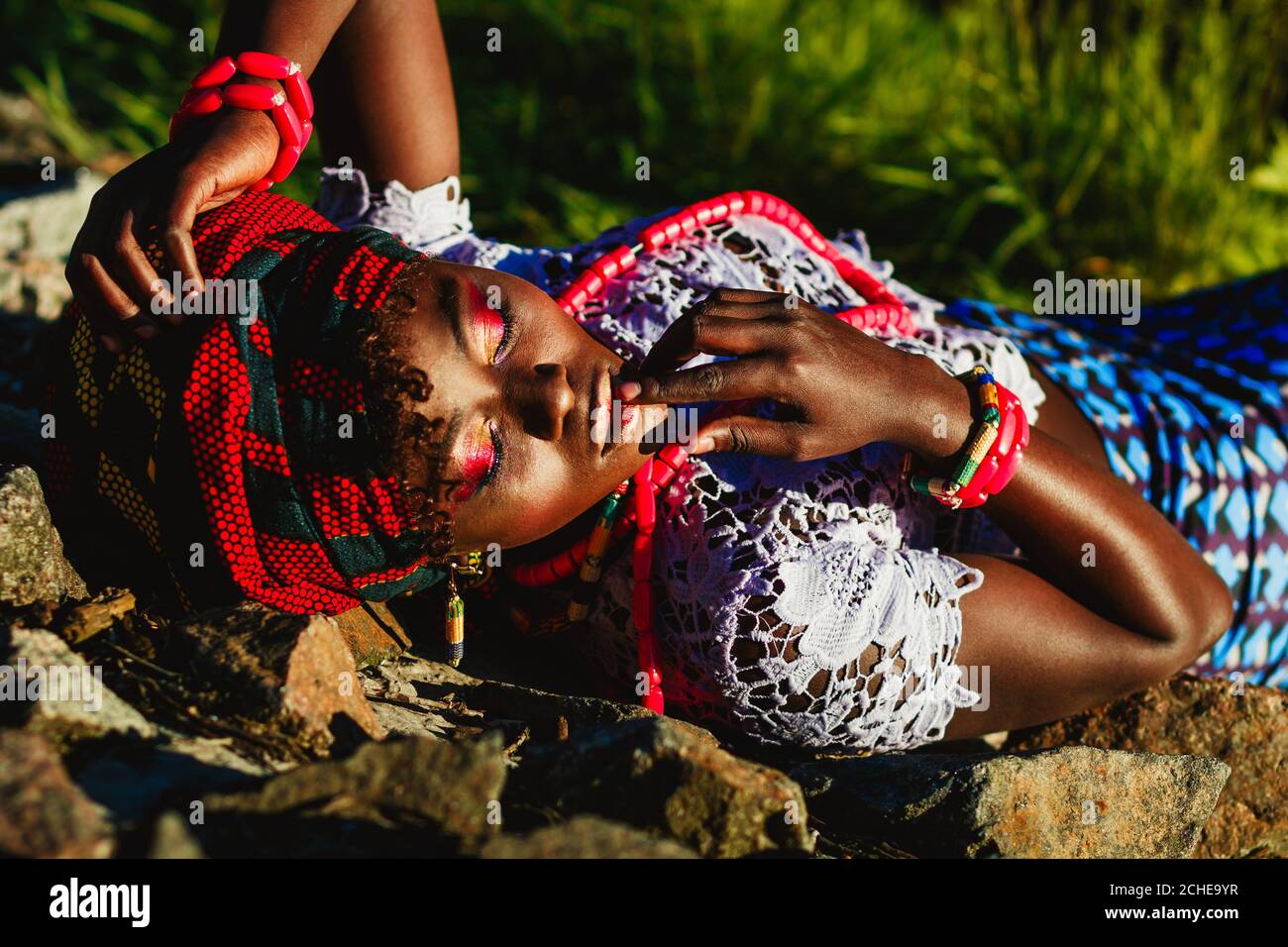 Foto de moda de modelo femenino joven africano en traje nacional, turbante y brillante de colores componen acostado en las piedras. Concepto turístico exótico Foto de stock