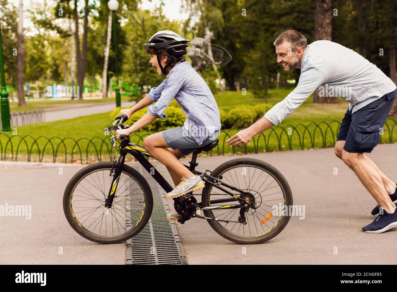 Hijo aprendiendo a montar en bicicleta con su padre feliz Foto de stock