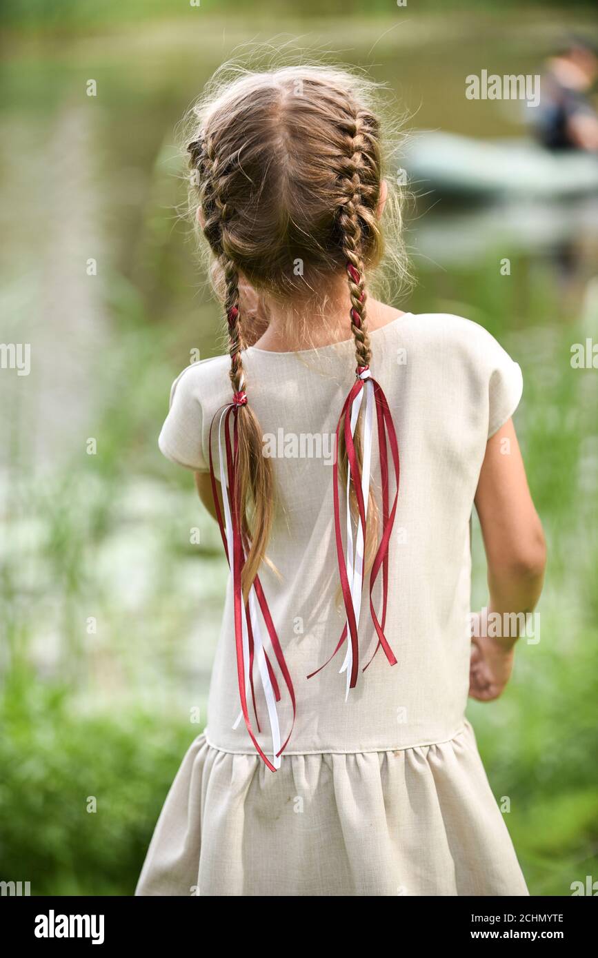 Una chica con trenzas en su cabello y cintas en los colores de una bandera  de letonia mira hacia el río, volviendo su espalda al fotógrafo Fotografía  de stock - Alamy