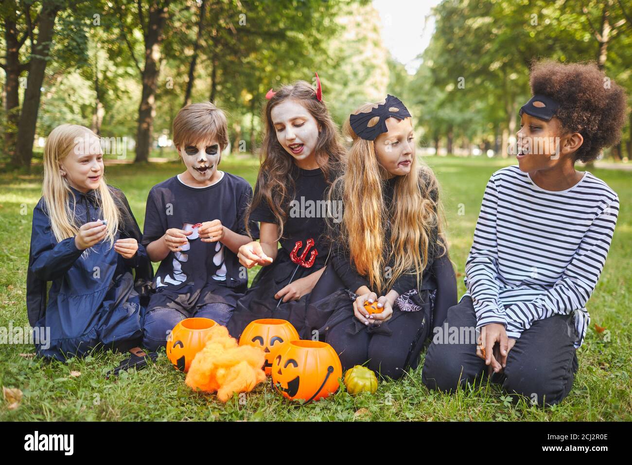 Retrato completo de un grupo multiétnico de niños comiendo dulces En Halloween al aire libre, mientras que el uso de trajes Foto de stock