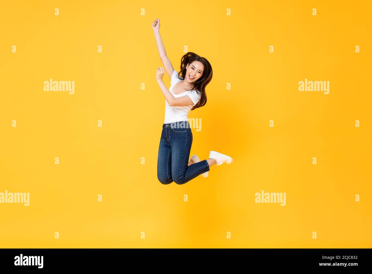 Retrato completo de una mujer asiática bonita sonriendo y saltando en medio del aire aislado sobre fondo amarillo Foto de stock