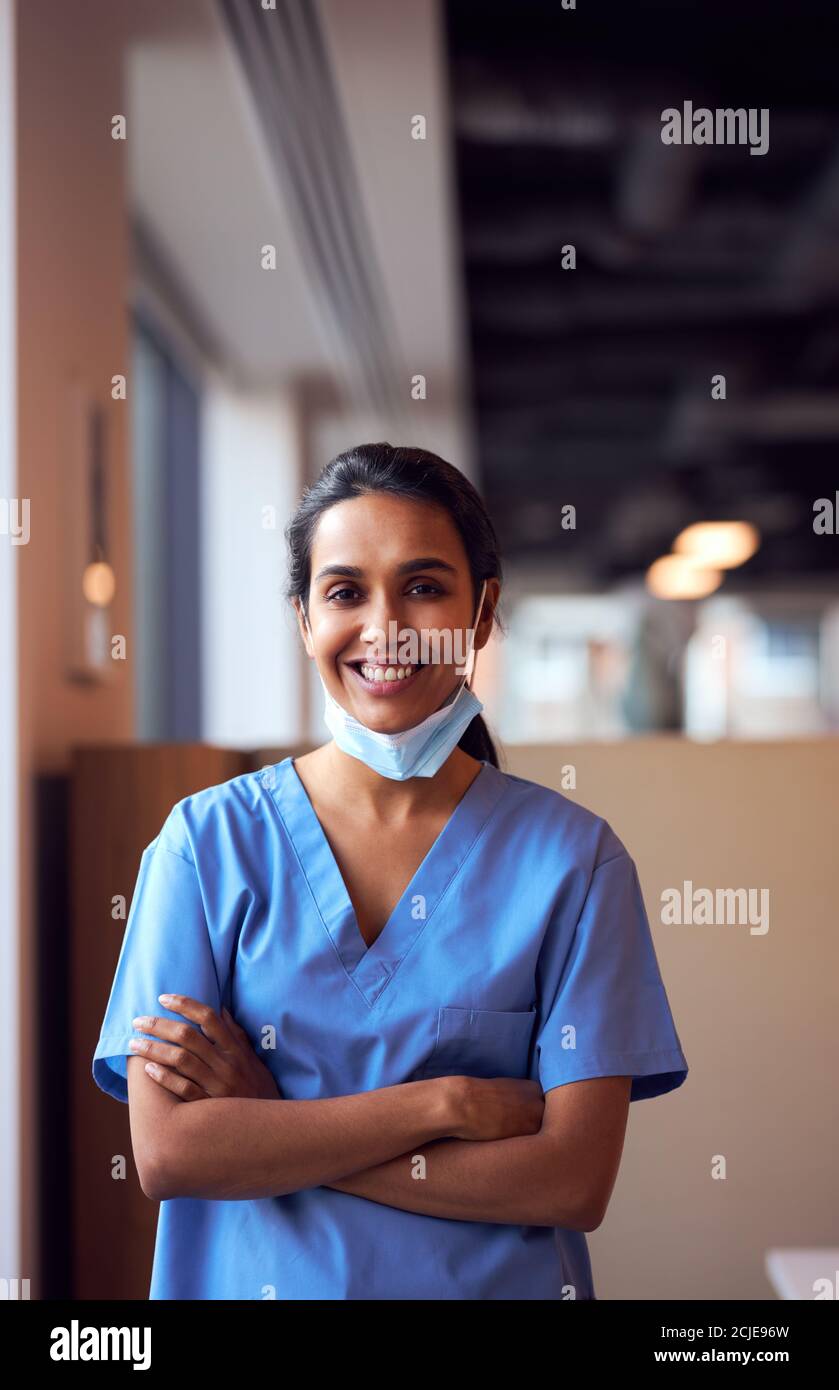 Mujer sonriente Doctor con máscara de cara usando Scrubs en ocupado Hospital durante la pandemia de Salud Foto de stock