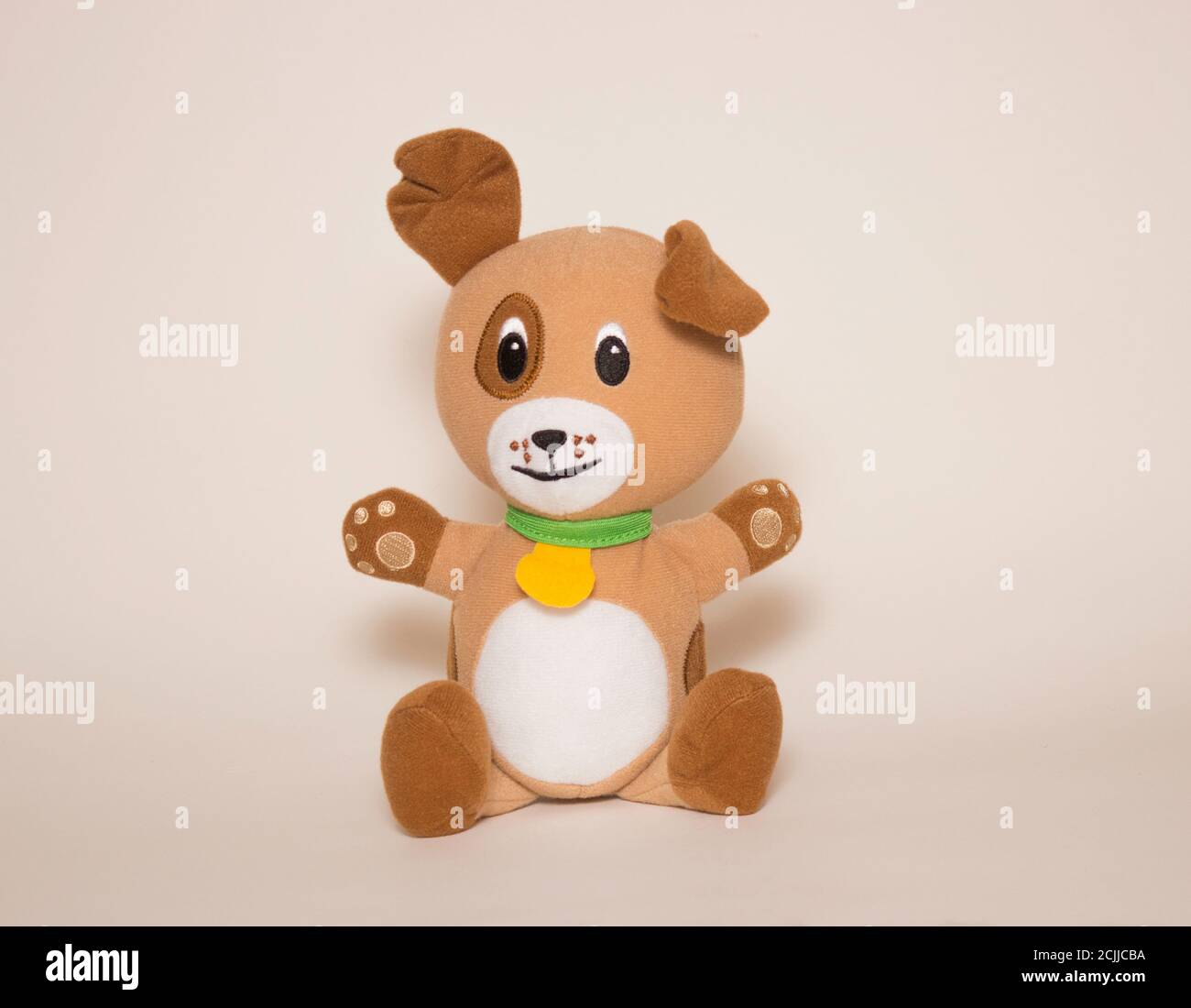 Un perro marrón de juguete se sienta sobre un fondo blanco. Juguetes para niños, animales de peluche suave. Foto de stock