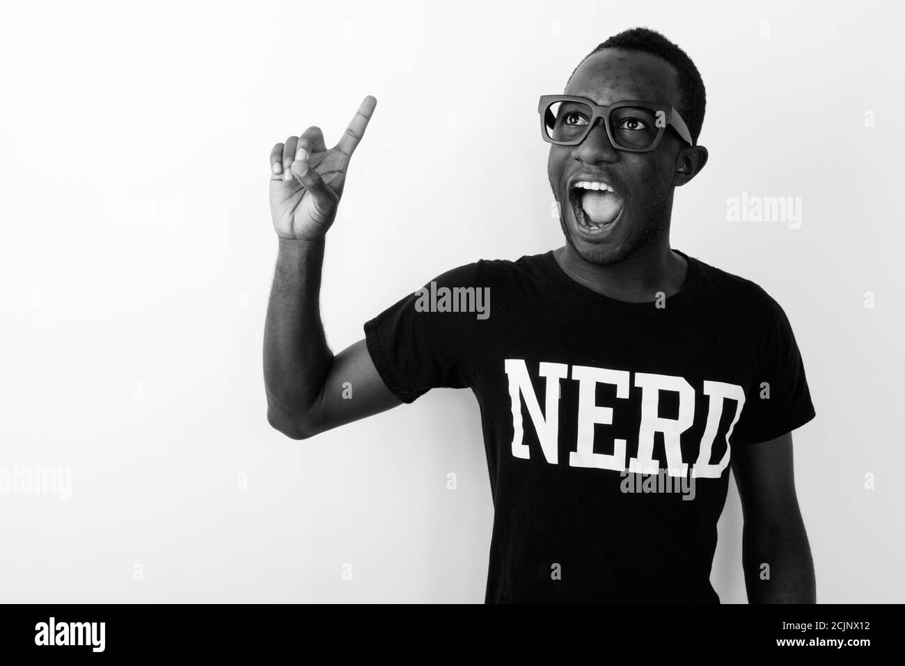 Joven feliz hombre geek africano con gran idea sonriendo y.. Apuntando con el dedo hacia arriba mientras llevas camisa Nerd Foto de stock