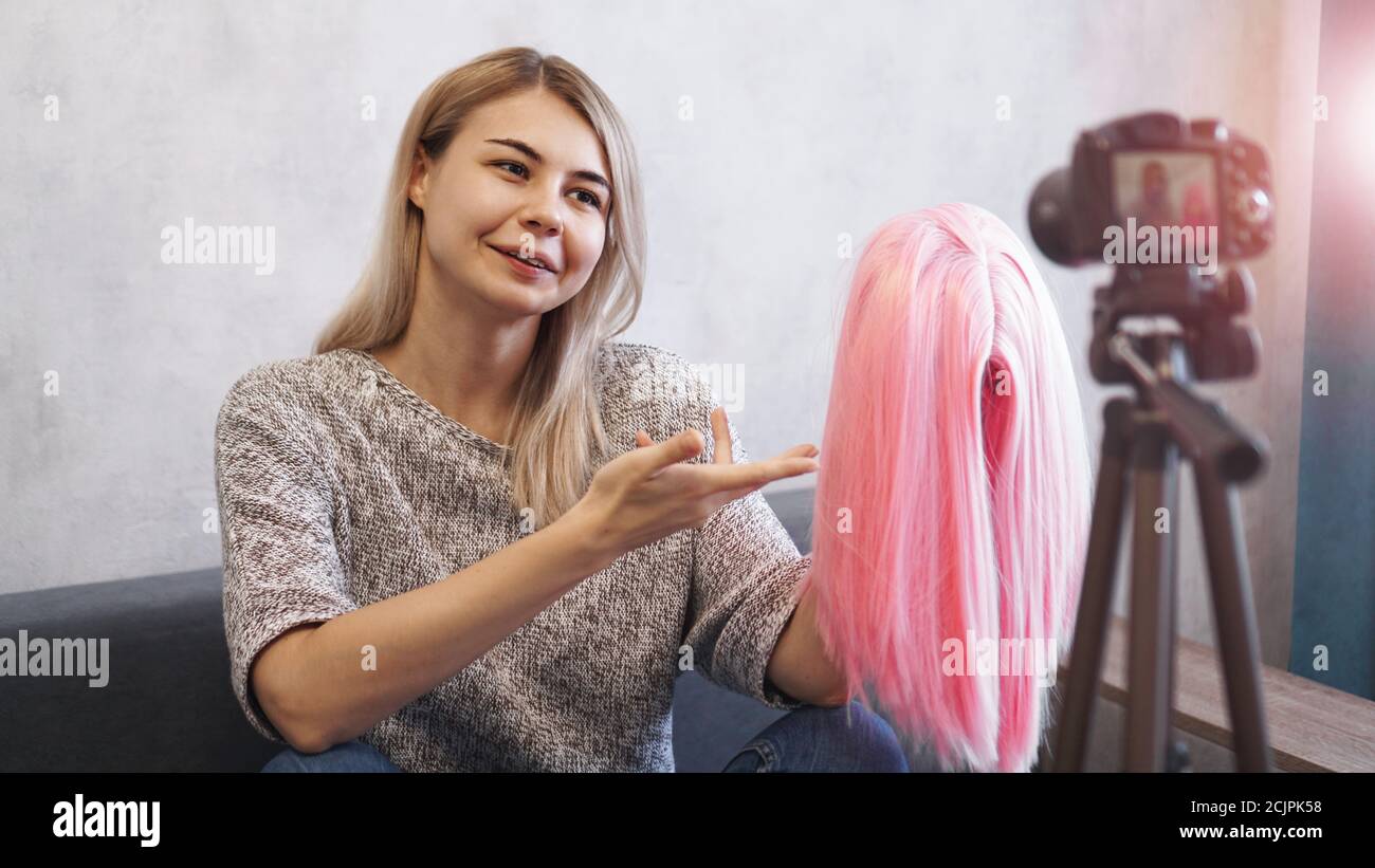 Mujer blogger graba vídeo. Habla de cortes de pelo y muestra una peluca rosa. Estilista y consultora de moda grabando la conferencia Foto de stock