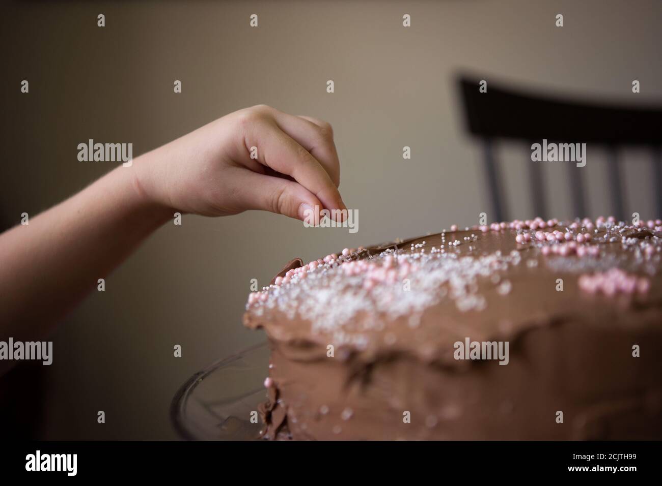 Primer plano de la mano de un niño decorar un chocolate congelado Pastel de cumpleaños con esprinkles Foto de stock