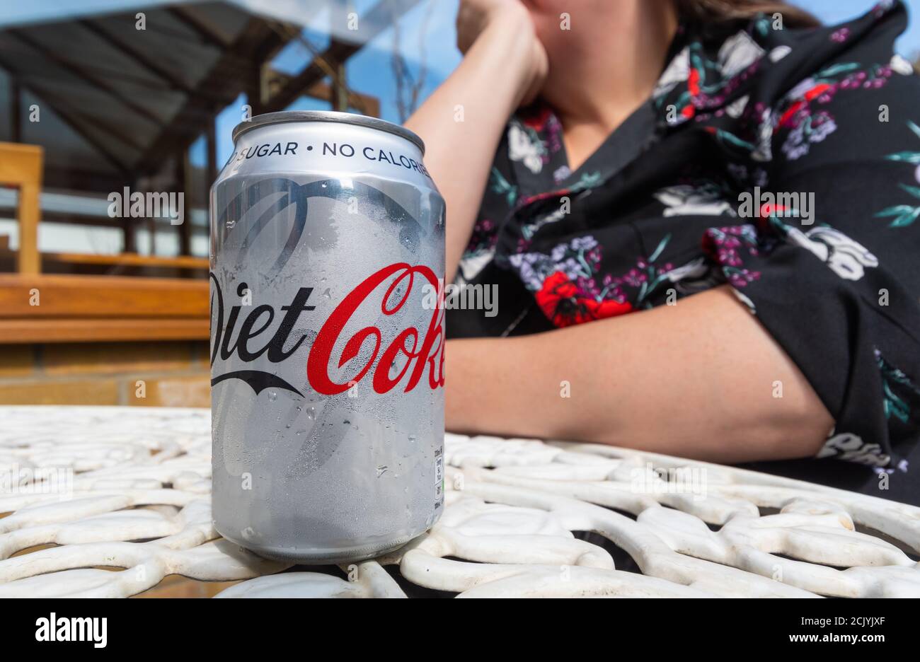 Mujer sentada en una mesa fuera en un día caluroso en verano con una lata de Coca-Cola dieta, en el Reino Unido. Foto de stock