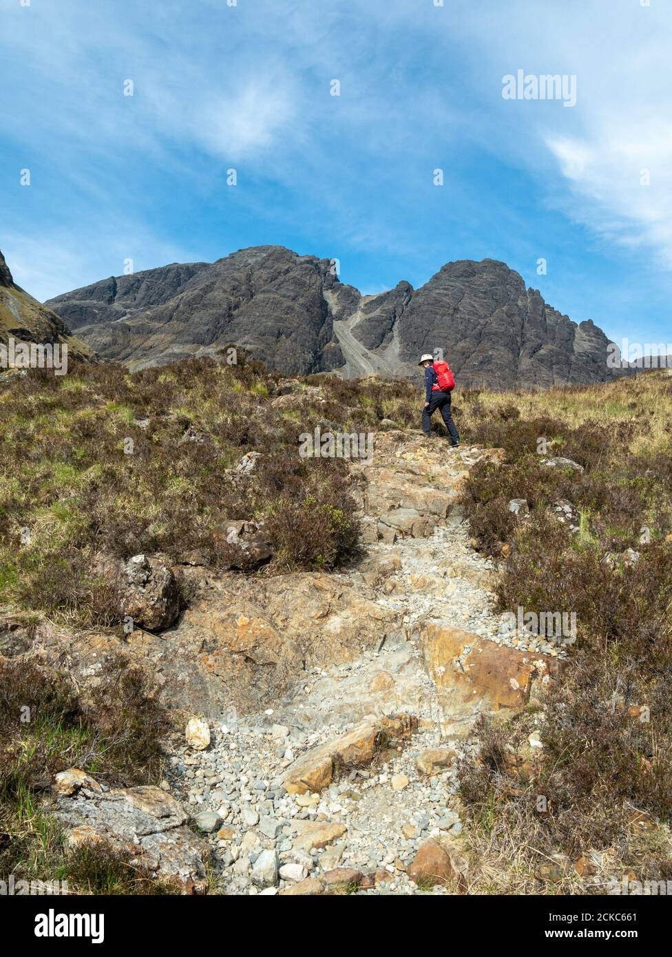 Caminante femenino con mochila ascendente camino de montaña en las laderas inferiores de Blaven en las Montañas de la Cuillin Negro, Isla de Skye, Escocia, Reino Unido Foto de stock
