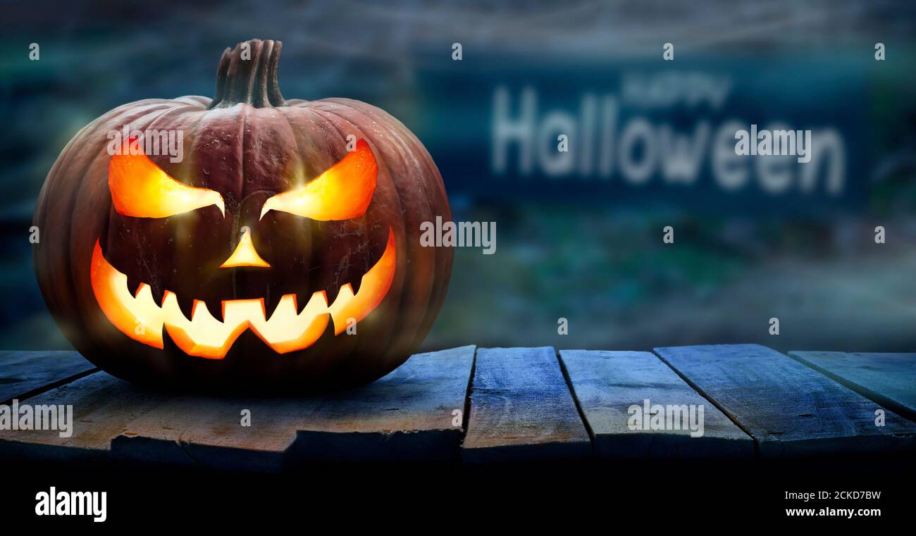 Una calabaza de halloween espeluznante, Jack o Lantern, con un rostro malvado y ojos en un banco de madera, mesa con un fondo de noche brumoso con espacio para el producto Foto de stock