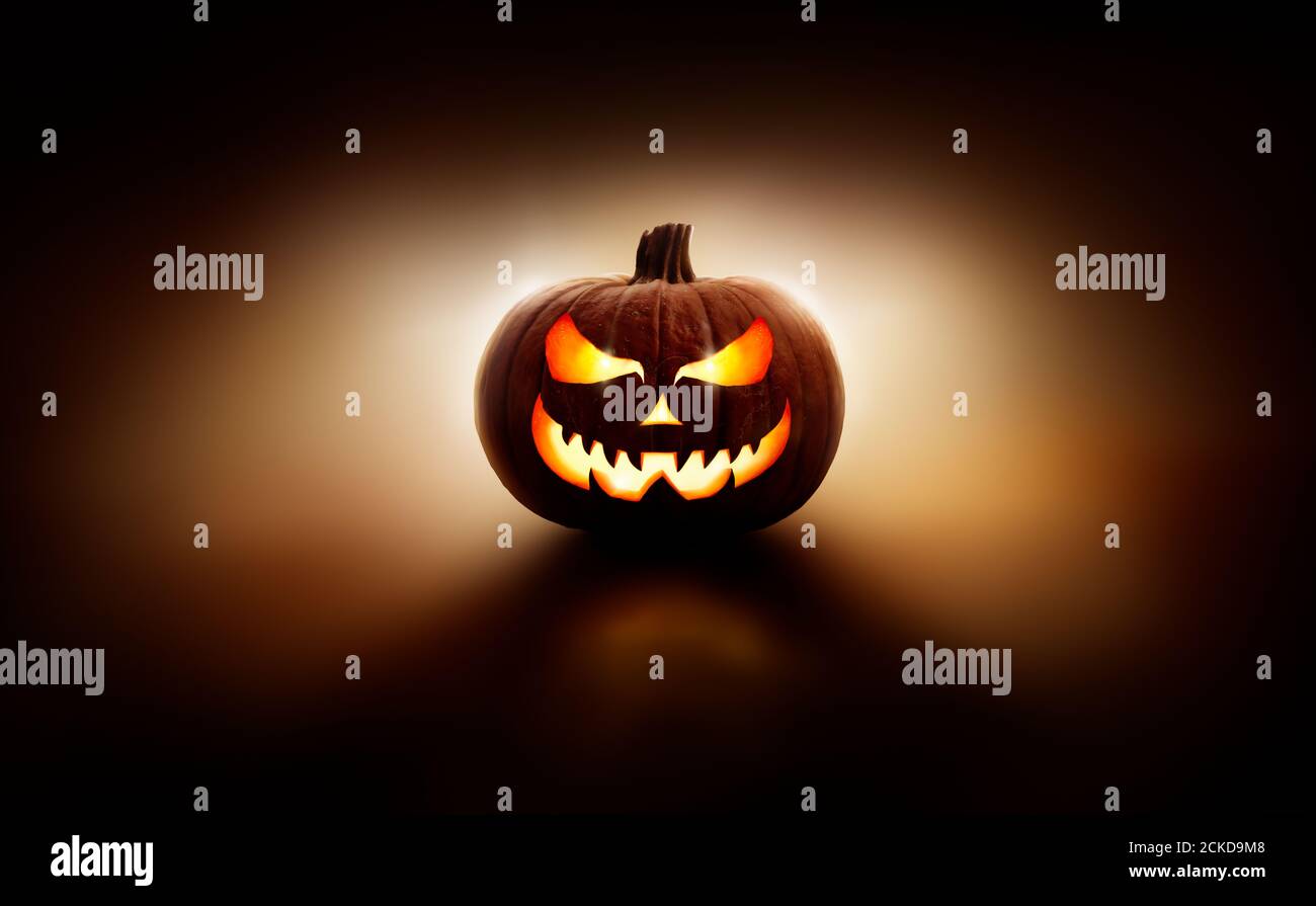 Una linterna de halloween retroiluminada, Jack o Lantern, con una cara malvada y espeluznante con ojos brillantes contra un fondo oscuro. Foto de stock