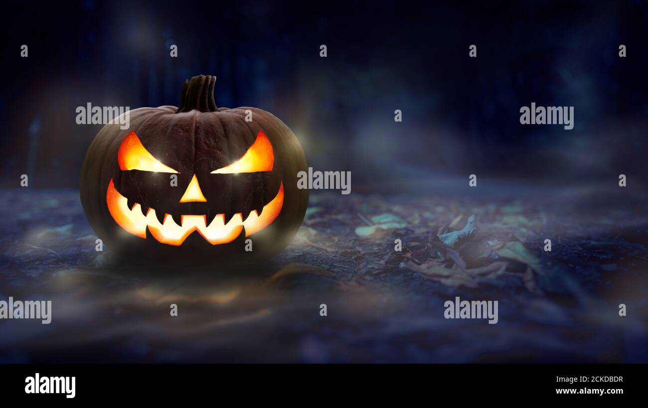 Una calabaza de halloween espeluznante, Jack o Lantern, con cara malvada y ojos brillantes en un suelo de bosque cubierto de hojas por la noche. Foto de stock