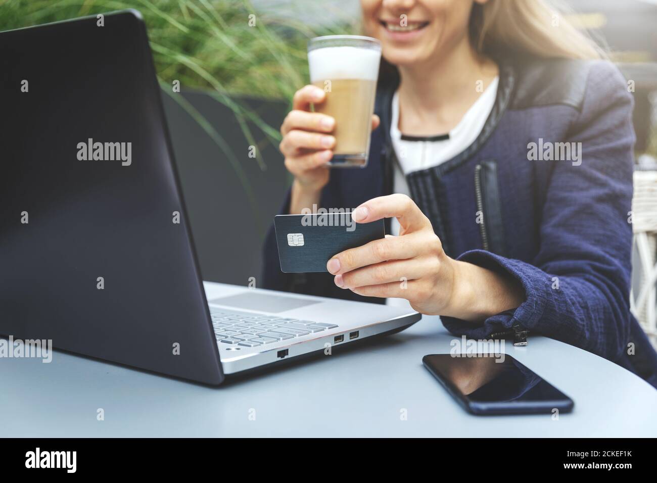 mujer sonriente sosteniendo la tarjeta de crédito en la mano y usando el ordenador portátil mientras bebía café en el café. compras en línea y concepto de pago Foto de stock
