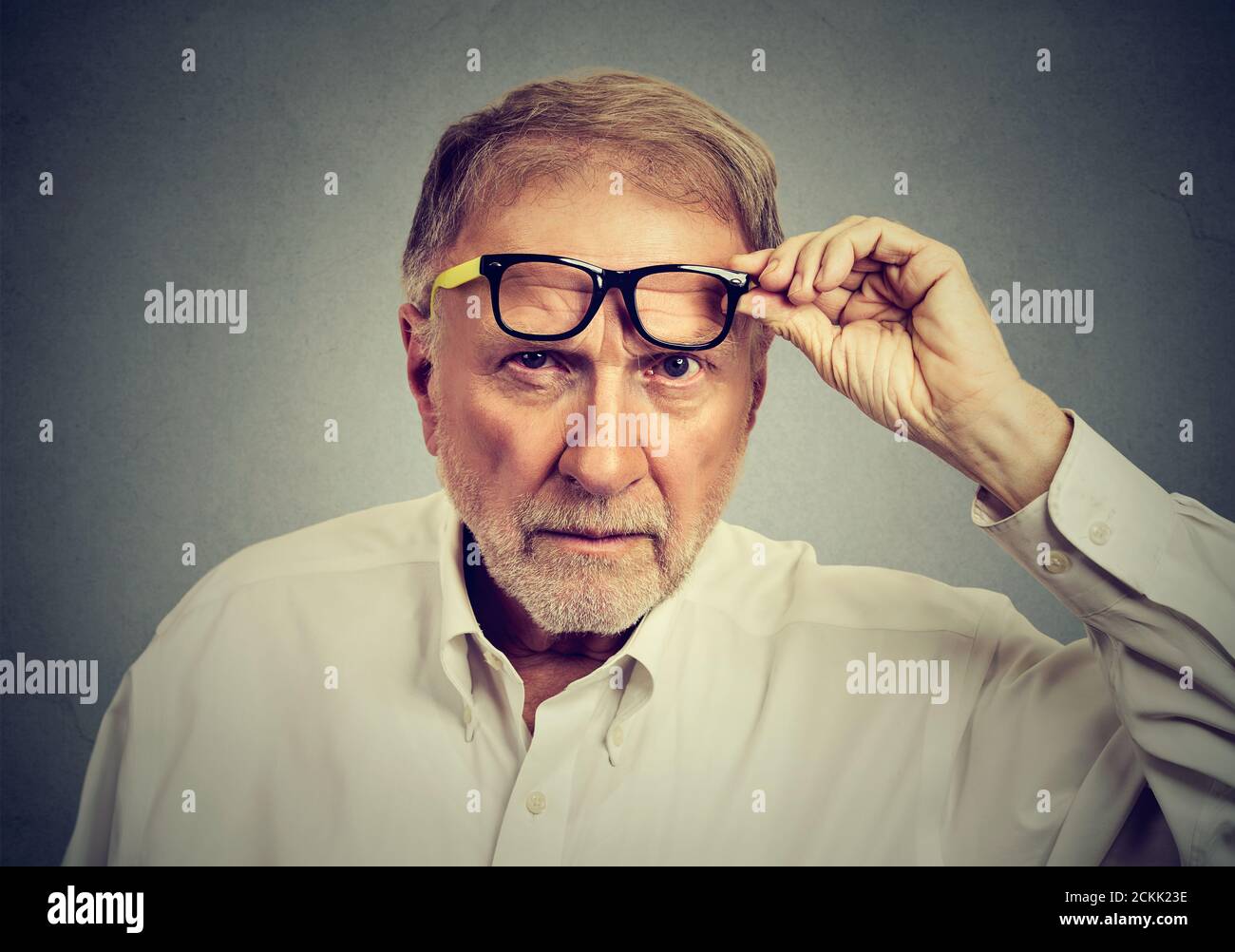 Hombre anciano escéptico con gafas que te miran aislado sobre fondo gris. Emociones humanas, lenguaje corporal Foto de stock