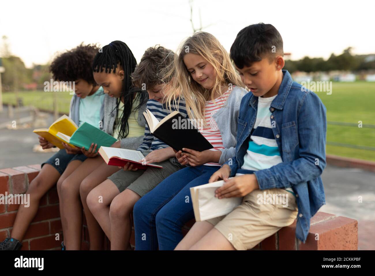 Grupo de niños leyendo libros mientras se sentaba en un ladrillo pared Foto de stock