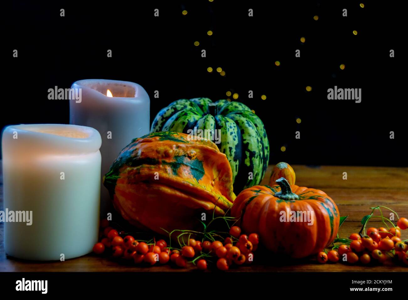 Composición decorativa hecha de calabazas, bayas de rowan y velas sobre mesa rústica de madera y fondo negro con bokeh. Verduras simbólicas de otoño Foto de stock