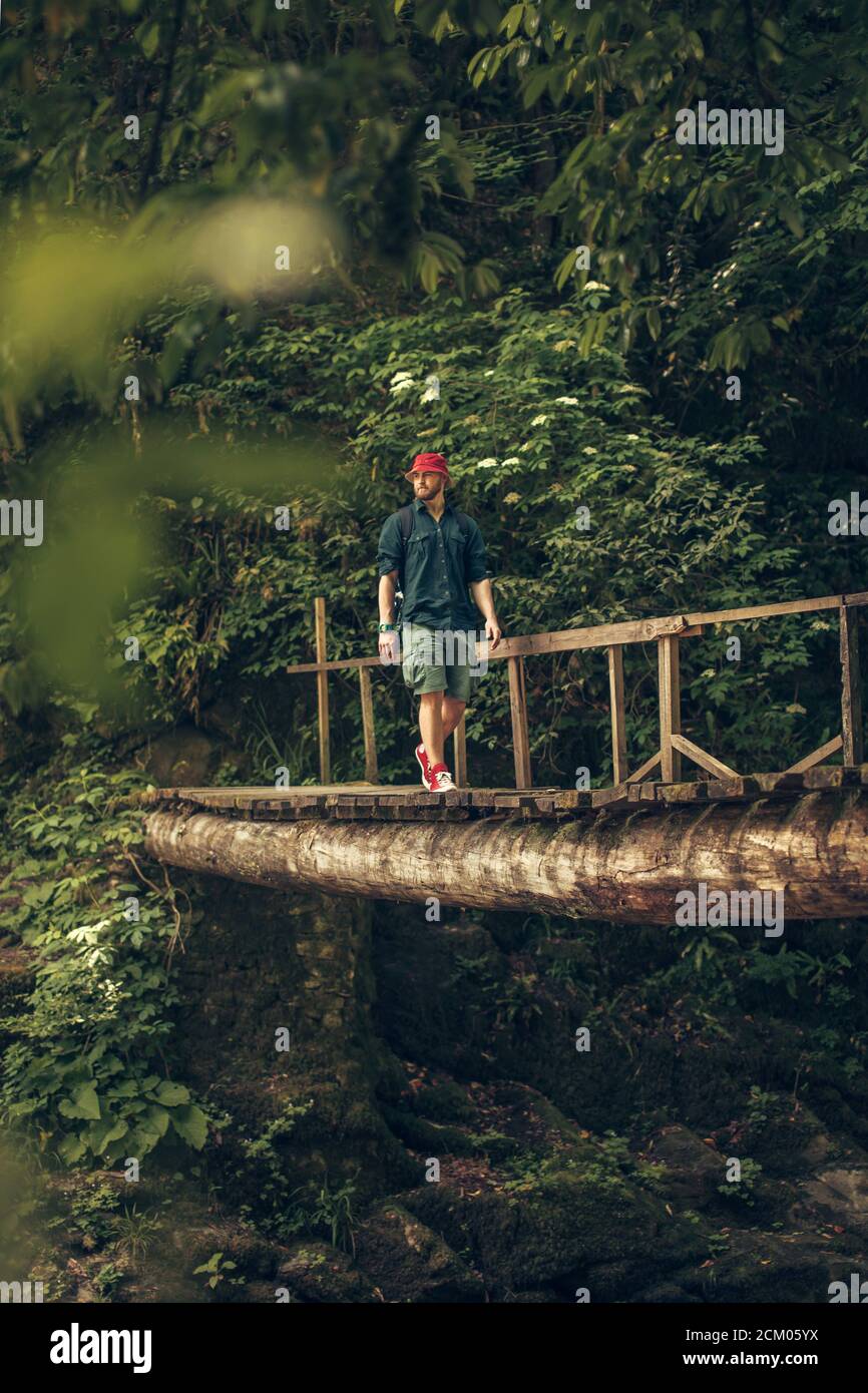 Hombre de senderismo con sombrero rojo y zapatillas de deporte rojas  caminando sobre un puente peatonal de madera en un bosque de hoja caduca en  la isla sueca Fotografía de stock -