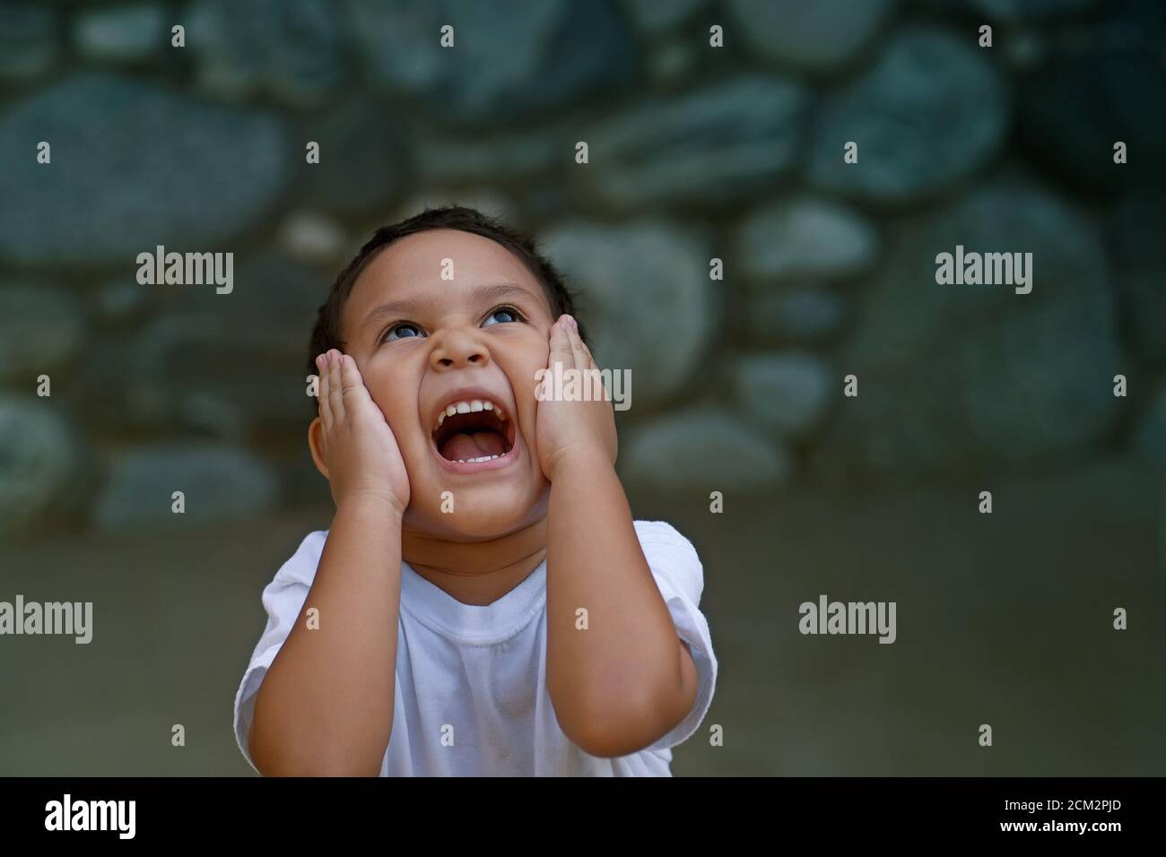 El preschooler latino abrumado con felicidad sostiene su cara con ambas manos y grita muy fuerte. Foto de stock