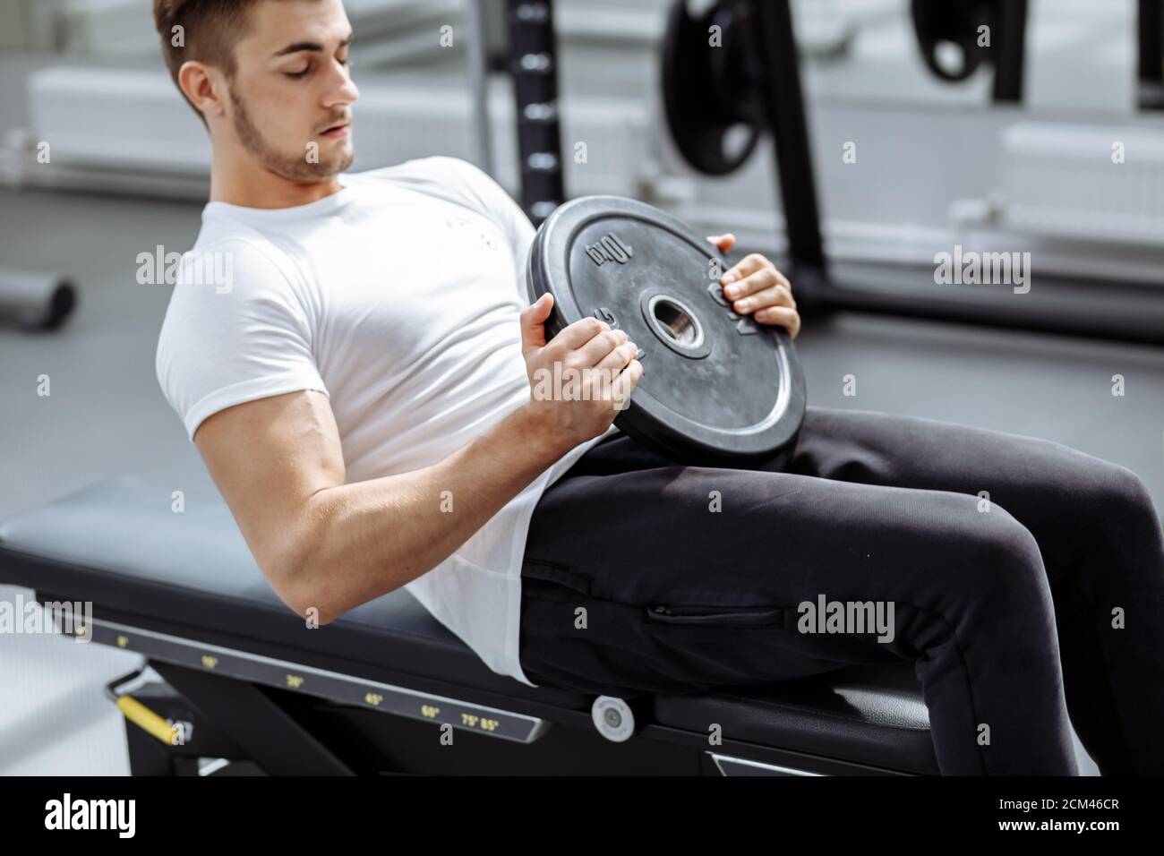 Tío musculoso en camiseta blanca haciendo sentarse ups en el gimnasio.  Joven atleta haciendo ejercicios en estómago moderno Fitness Studio  Fotografía de stock - Alamy