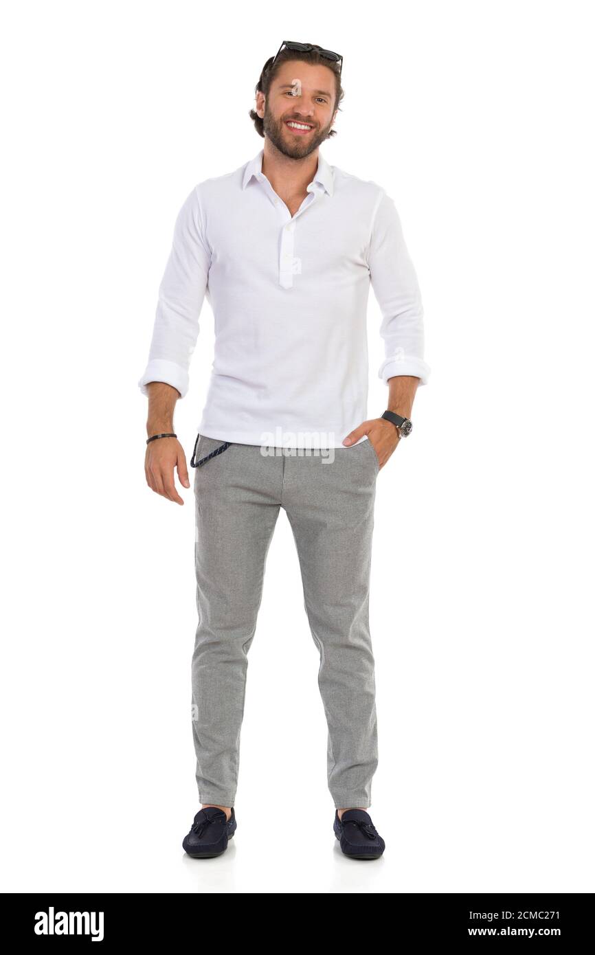 Un hombre elegante y guapo con camisa blanca, pantalones grises y mocasines  está de pie relajado con la mano en el bolsillo, mirando la cámara y  sonriendo. Longitud completa s Fotografía de