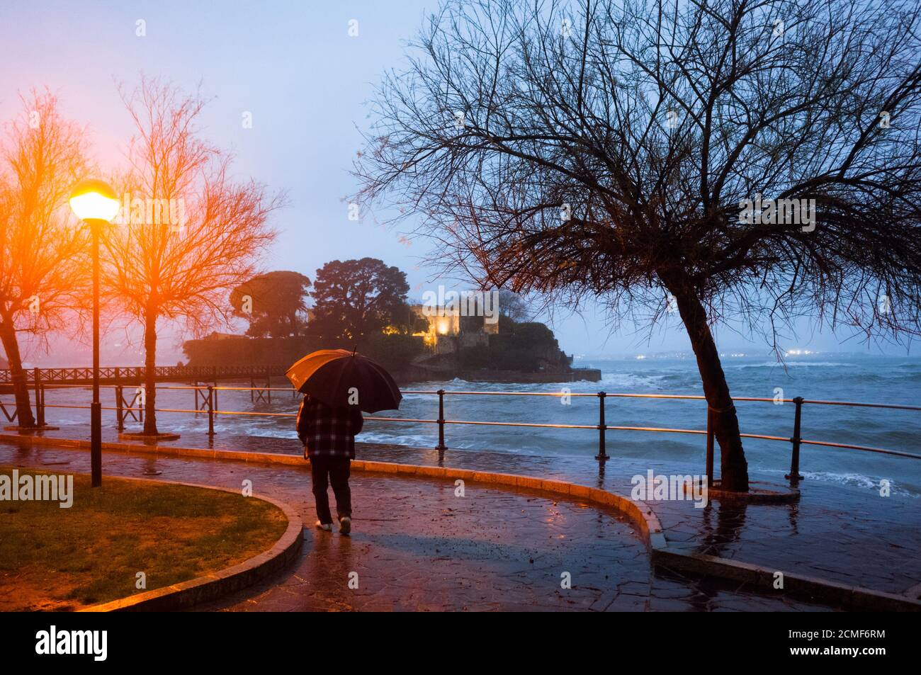 Oleiros, provincia de A Coruña, Galicia, España - 11 de febrero de 2020 : un hombre que sostiene un paraguas camina en la orilla pasando por el ingenio isleño de Santa Cristina Foto de stock