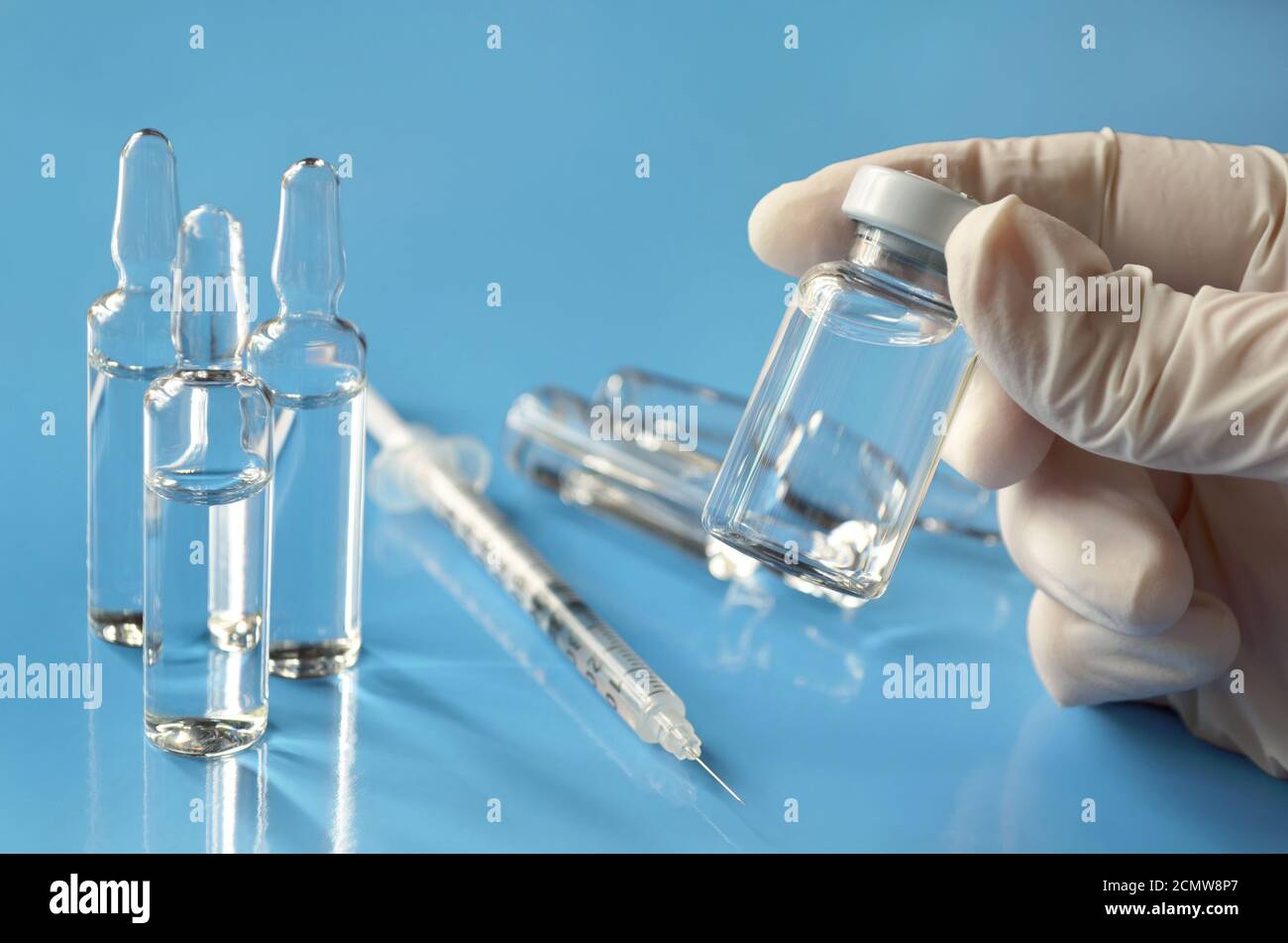Vial médico de medicamento en manos de un profesional médico sobre un fondo azul claro con ampollas de vidrio y una jeringa desechable. Foto de stock
